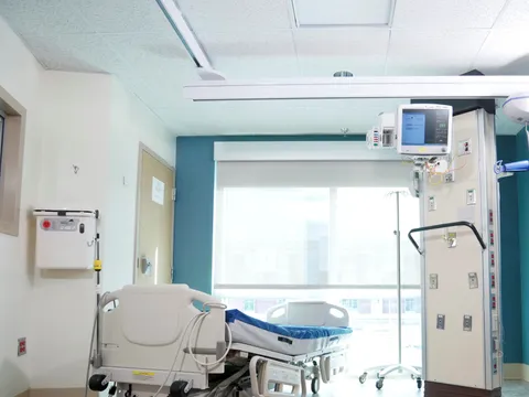 A bright intensive care room with a bed beside a service column carrying a monitor and wall outlets