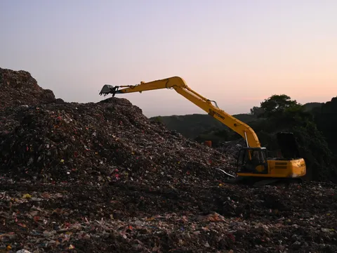 An excavator working on a landfill at dusk