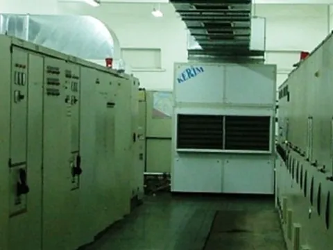 An industrial air conditioner standing at the end of an electrical room, between rows of switchgear panels